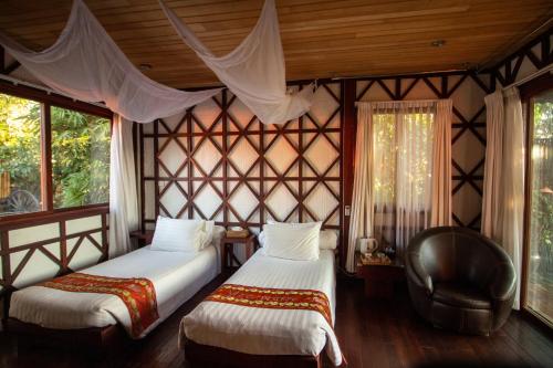 um quarto com 2 camas, uma cadeira e janelas em ViewPoint Ecolodge em Nyaung Shwe