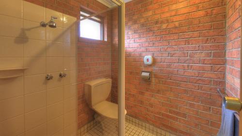 a bathroom with a toilet and a brick wall at Moama Central Motel in Echuca