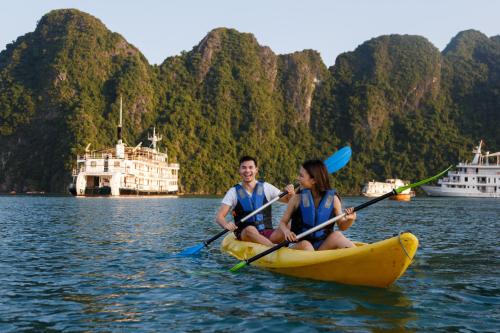 a man and woman in a kayak on the water with two boats at Emeraude Classic Cruises in Ha Long