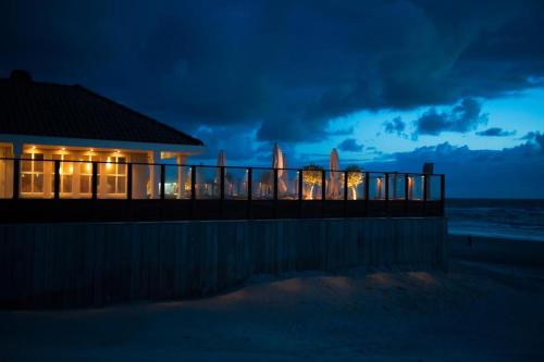a house on the beach at night with lights at 't STRANDHUYS en DE VUURTOREN, met eigen KEUKEN, ZONNIG TERRAS nabij DORP, DUINEN en STRAND, Incl verwarmd binnen ZWEMBAD in Hollum