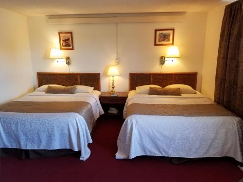 two beds in a hotel room with two lamps at Sleep For Less Motel in Sidney