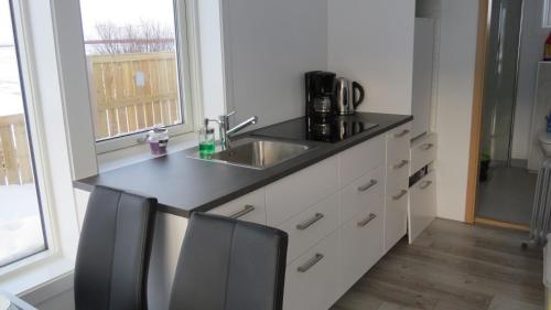 uma cozinha com um lavatório e um balcão com 2 cadeiras em Hvammur 2 Bjarg with private hot tub em Drangsnes