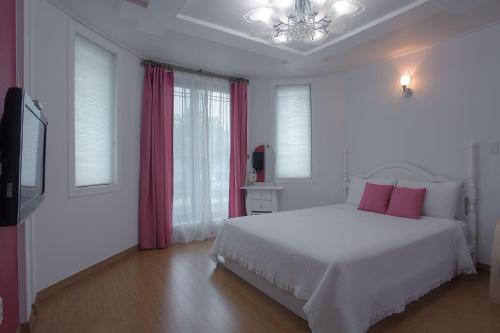 a white bedroom with a white bed and pink pillows at Forest of Color Pension in Hongcheon