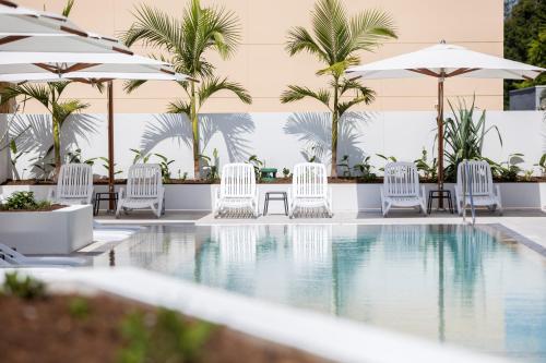a pool with white chairs and umbrellas at Ruby Gold Coast by CLLIX in Gold Coast