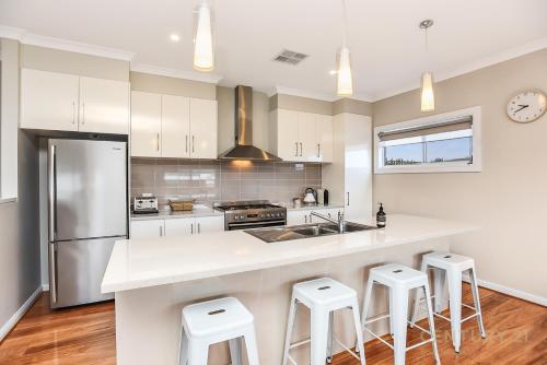 una cocina con armarios blancos y una barra con taburetes en Seahaven - Sellicks Beach - C21 SouthCoast Holidays en Sellicks Beach