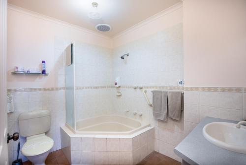 a bathroom with a tub and a toilet and a sink at Mid City Motel in Mount Gambier