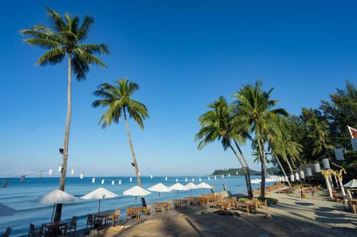 a beach with tables and palm trees and the ocean at Santhiya Koh Chang Resort in Ko Chang