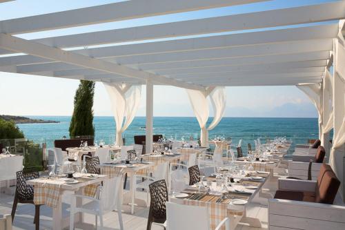 a dining area with white tables and chairs and the ocean at Mareblue Beach in Agios Spyridon Corfu