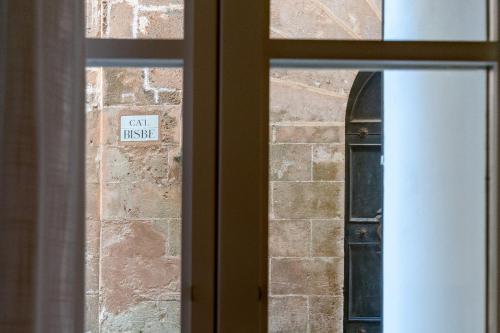 a sign on a brick wall seen through a window at Divina Suites Hotel Boutique - Adults only in Ciutadella