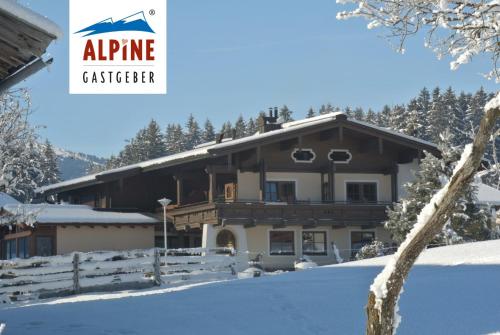 a house in the snow with the alpine cottier sign at Gästehaus Stotter in Neukirchen am Großvenediger