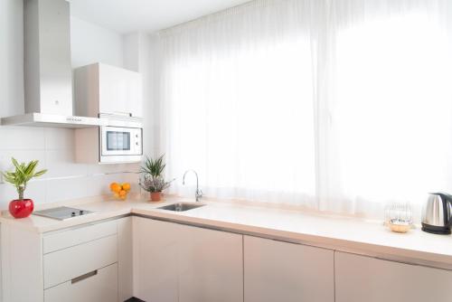 a kitchen with white cabinets and a large window at Suites Campo del Príncipe by Maxi Hoteles in Granada