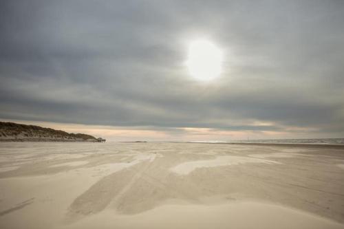 a sandy beach with the sun in the sky at 't STRANDHUYS en DE VUURTOREN, met eigen KEUKEN, ZONNIG TERRAS nabij DORP, DUINEN en STRAND, Incl verwarmd binnen ZWEMBAD in Hollum