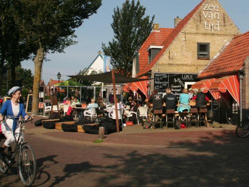 a woman riding a bike down a street with people sitting at tables at 't STRANDHUYS en DE VUURTOREN, met eigen KEUKEN, ZONNIG TERRAS nabij DORP, DUINEN en STRAND, Incl verwarmd binnen ZWEMBAD in Hollum