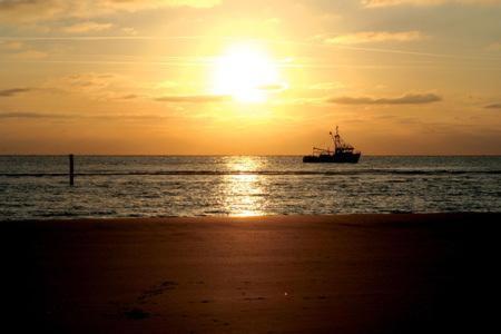 a boat in the ocean with the sun in the sky at 't STRANDHUYS en DE VUURTOREN, met eigen KEUKEN, ZONNIG TERRAS nabij DORP, DUINEN en STRAND, Incl verwarmd binnen ZWEMBAD in Hollum