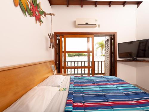 a bedroom with a bed and a tv and a window at Pousada Pé Na Areia in Caraguatatuba