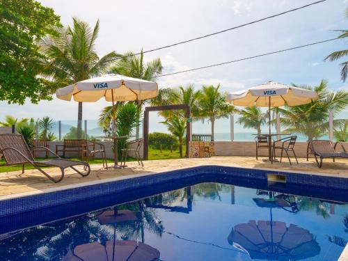 a swimming pool with chairs and umbrellas next to the ocean at Pousada Pé Na Areia in Caraguatatuba