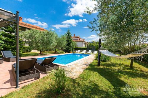 a swimming pool with chairs and a hammock next to a house at Family Vacation Villa in Žbandaj