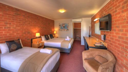 a hotel room with two beds and a brick wall at Pevensey Motor Lodge in Echuca