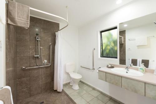 a bathroom with a shower and a toilet and a sink at Kauri Park Motel in Kerikeri