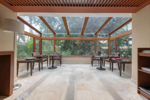 a conservatory with tables and chairs in a room with large windows at Wyndham Garden Guadalajara Expo Plaza del Sol in Guadalajara