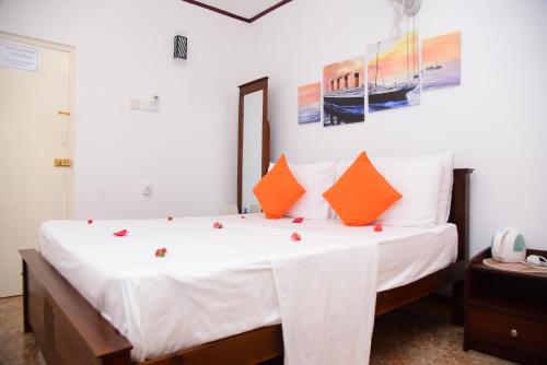 a bedroom with a bed with white sheets and orange pillows at White Villa Airport Transit Hotel in Katunayake