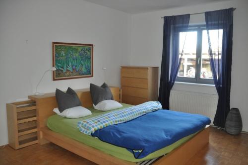 Schlafzimmer mit einem Bett mit blauer Bettwäsche und einem Fenster in der Unterkunft Ferienwohnung Alpenseepark in Mondsee