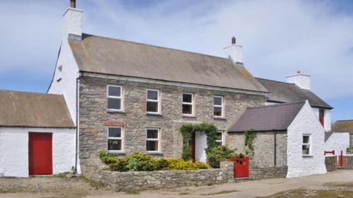 uma antiga casa de pedra com uma porta vermelha e branca em Treleddyn Farmhouse em St. Davids