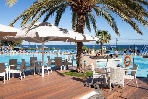 un complejo con piscina y terraza con sillas y sombrillas en Grand Teguise Playa en Costa Teguise