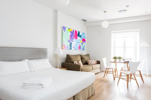 a white bedroom with a bed and a living room at Suites Sevilla Plaza in Seville