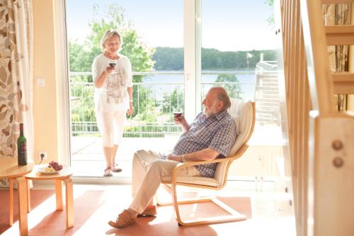 an older man sitting in a chair while a woman walks by a door at Aparthotel Seepanorama in Mirow