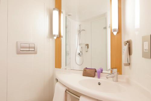 uma casa de banho branca com um lavatório e um espelho em ibis London Luton Airport em Luton