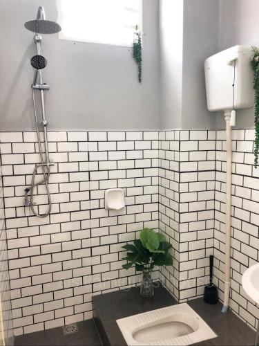 a white tiled bathroom with a toilet and a plant at Sisikami Guesthouse in Changlun