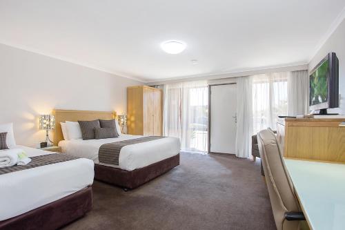 a hotel room with two beds and a flat screen tv at Mid City Motel Warrnambool in Warrnambool