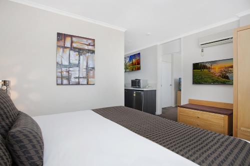a white bedroom with a bed and a kitchen at Mid City Motel Warrnambool in Warrnambool
