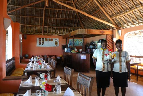 two men standing in front of a restaurant with tables at Blue Oyster Hotel in Jambiani
