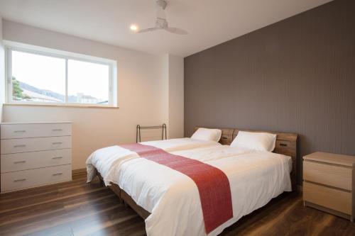 a bedroom with a bed and a dresser and a window at Hakuba Downtown Apartments in Hakuba