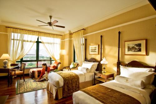 una mujer sentada en una habitación de hotel con dos camas en The Majestic Malacca Hotel - Small Luxury Hotels of the World en Melaka