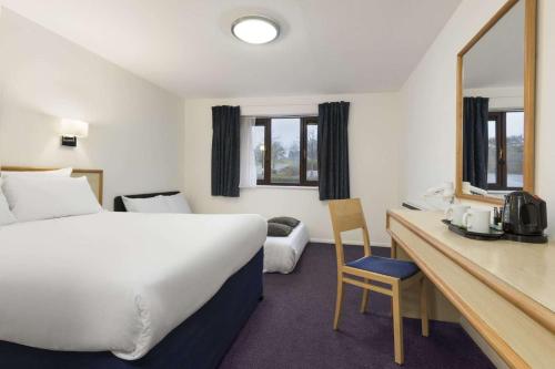 a hotel room with a bed and a desk with a mirror at Days Inn Bridgend Cardiff in Bridgend
