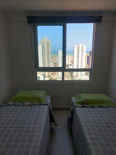 two beds in a room with a large window at Essencial Manaíra in João Pessoa