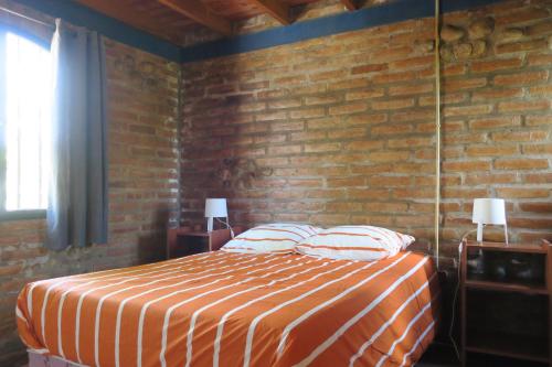 sypialnia z łóżkiem i ceglaną ścianą w obiekcie Cabañas A la Maison w mieście Mina Clavero