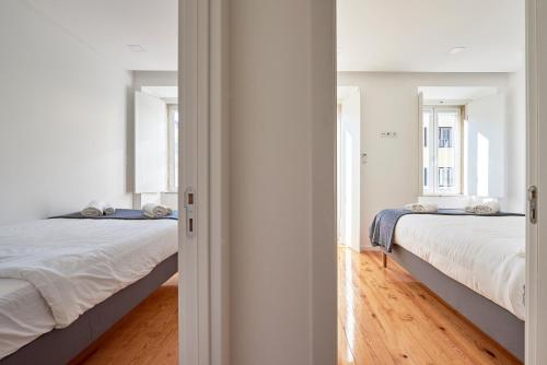 リスボンにあるCasa Eclea Lisbon Belem Design Apartmentの白い壁とウッドフロアの客室で、ベッド2台が備わります。