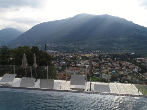 a swimming pool with chairs and umbrellas and a city at La Pergola PanoramaSuites in Tirolo