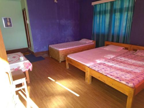 two beds in a room with purple walls and wooden floors at Vamoose Red Panda in Sombāri