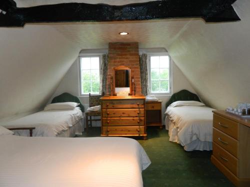 a attic bedroom with two beds and a dresser with a mirror at The Cedars Hotel in Stowmarket