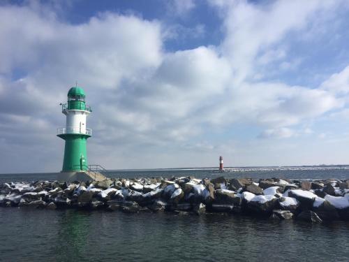 a green and white lighthouse on the water with a flock of birds at Hotel Am Alten Strom in Warnemünde