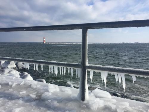 a view of the ocean with ice on a fence and a lighthouse at Hotel Am Alten Strom in Warnemünde