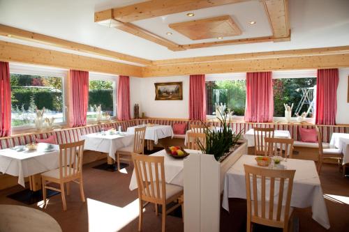 un restaurant avec des tables blanches, des chaises et des fenêtres dans l'établissement Pension Lärchenhof, à Naturno
