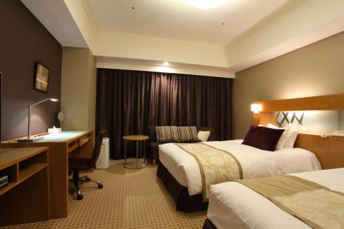 a hotel room with two beds and a desk at Hotel Metropolitan Nagano in Nagano