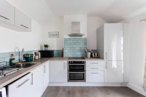 a white kitchen with white cabinets and a sink at Beautiful Two Bed Mumbles Flat - with parking space in The Mumbles