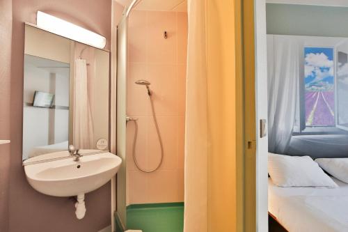 een badkamer met een wastafel en een spiegel naast een bed bij B&B HOTEL Montélimar Nord in Les Tourrettes